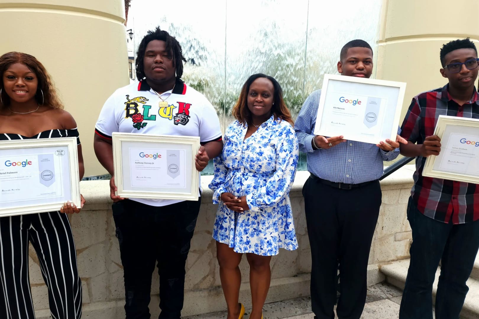 Three people holding up framed pictures in front of a building.